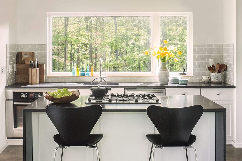 A modern kitchen with a large window looking into the forest.